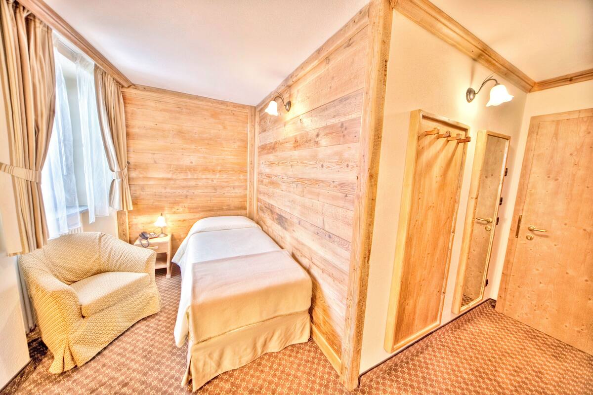 A room with wooden walls, a bed, a chair, a nightstand, and a door.