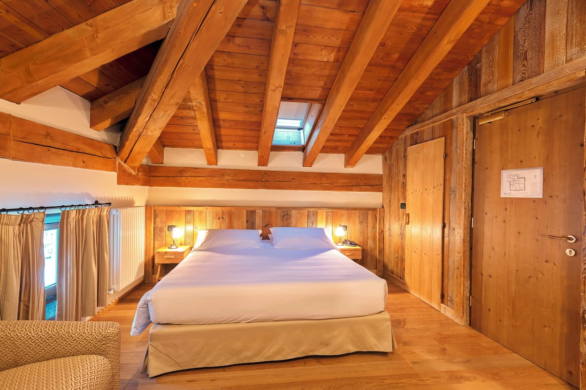 A wooden-paneled bedroom with a large bed, a nightstand with a lamp, and a door with a sign.