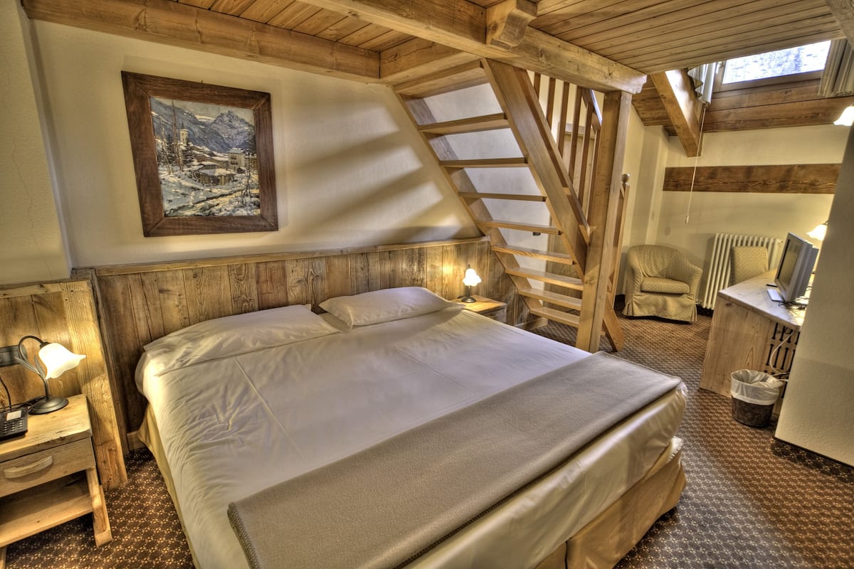 A bedroom with a wooden bed, a nightstand with a lamp, a framed picture on the wall, and a wooden ladder.