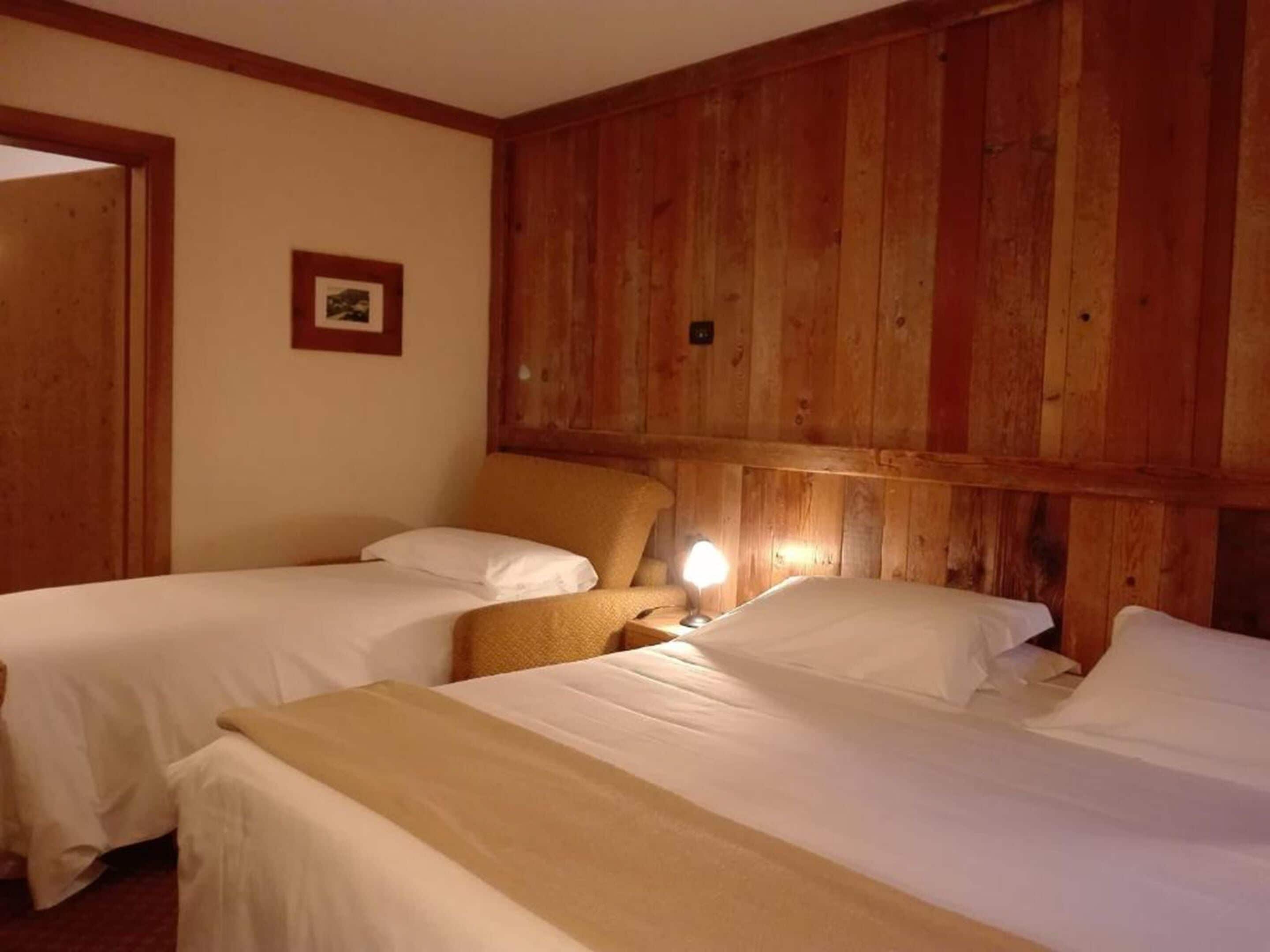 A room with two beds, wooden paneling on the walls, and a small table with a lamp.