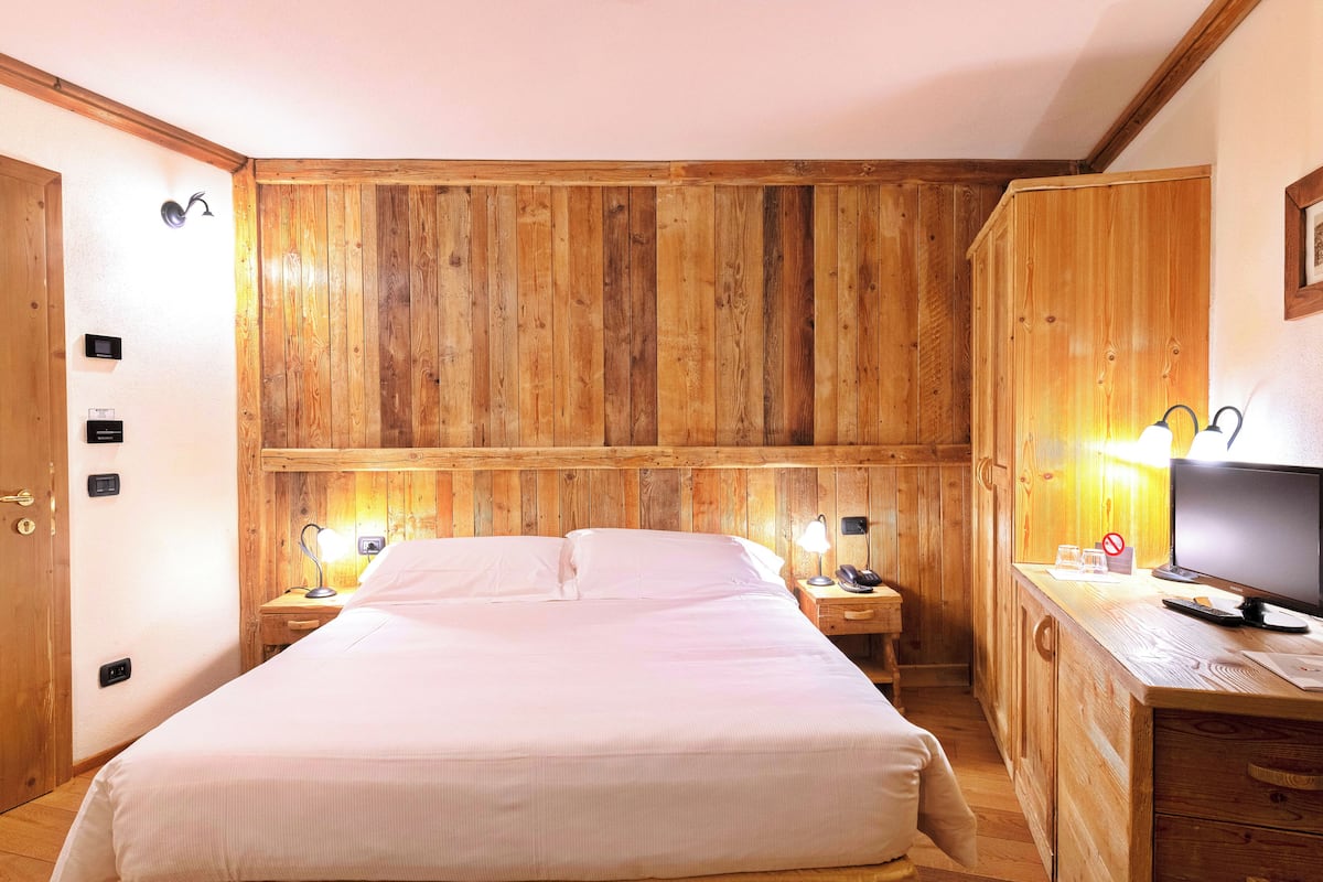 A wooden-paneled room with a bed, bedside lamps, a desk with a computer, and a television.