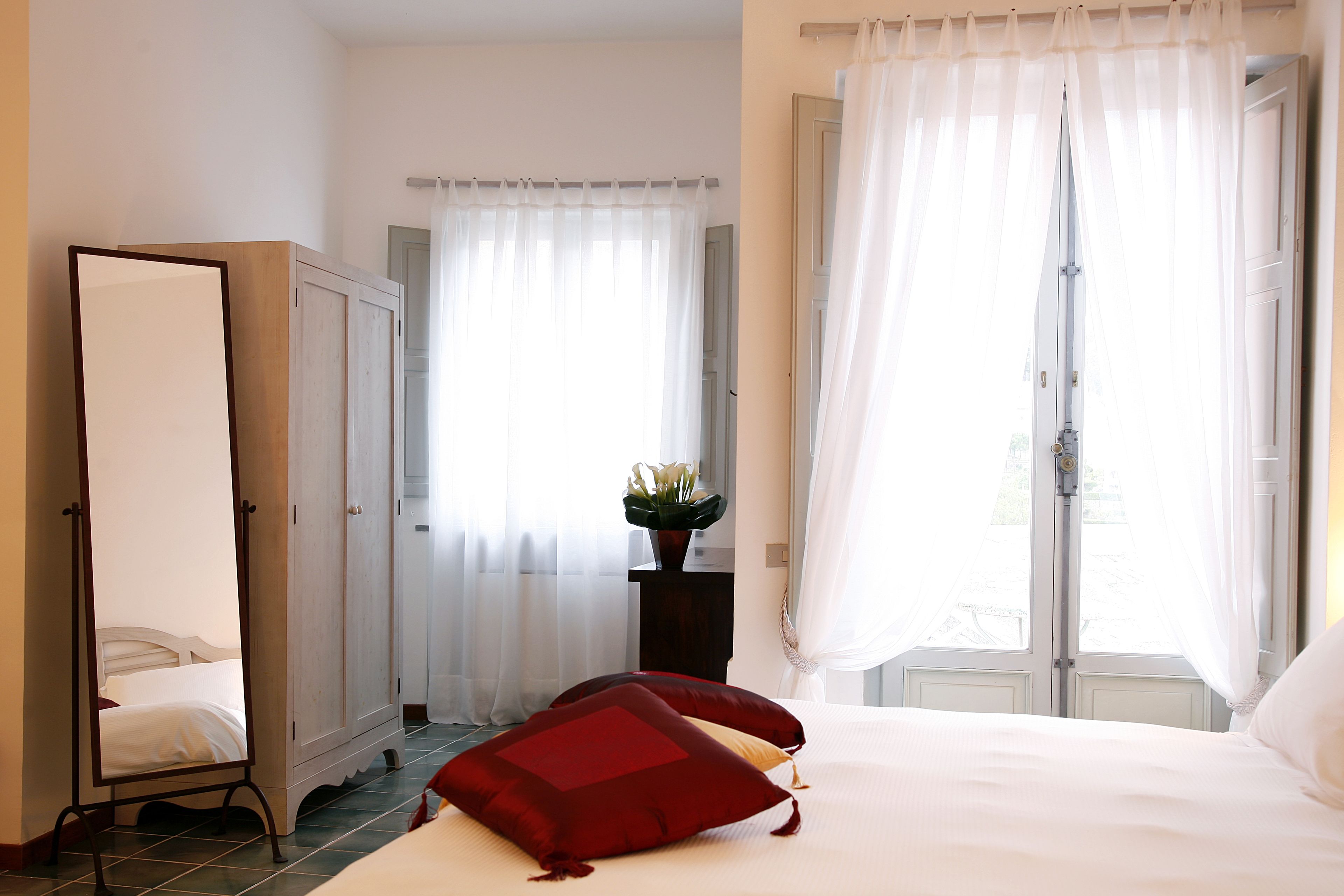 A bedroom with a bed, a wardrobe, a mirror, and a window with curtains.