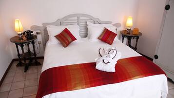 A neatly made bed with a red and white blanket, two bedside lamps, a telephone, and a pair of slippers on the floor.