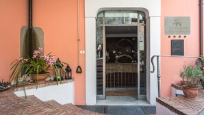 Entrada de un edificio con puerta de vidrio, una planta en maceta y una placa en la pared.