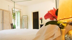 Un dormitorio con cama, mesita de noche y un jarrón con flores.