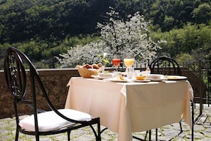A table set outdoors with a white tablecloth, a basket of bread, and two glasses of juice.