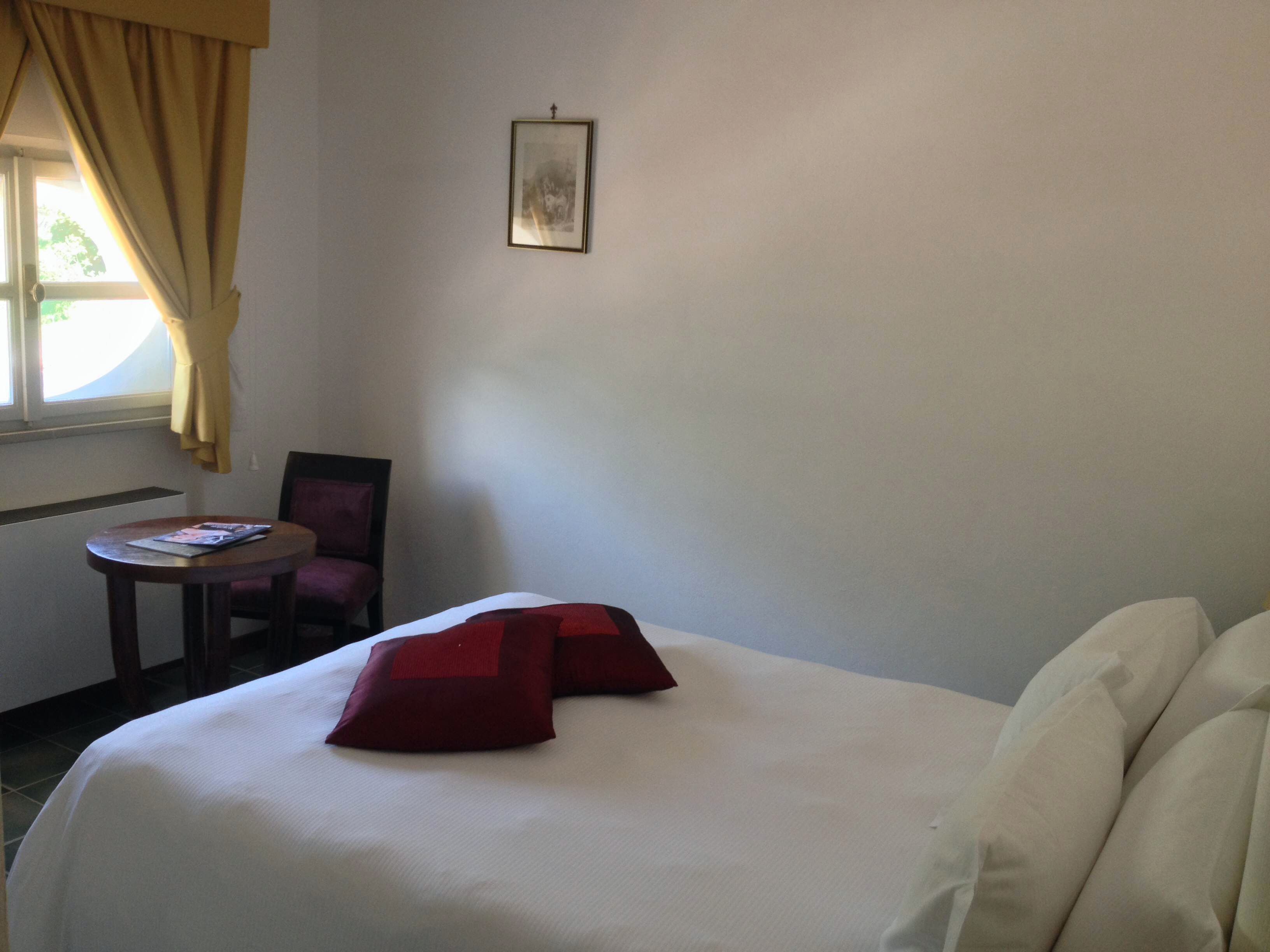 A hotel room with a bed, a small table, a chair, and a window with curtains.