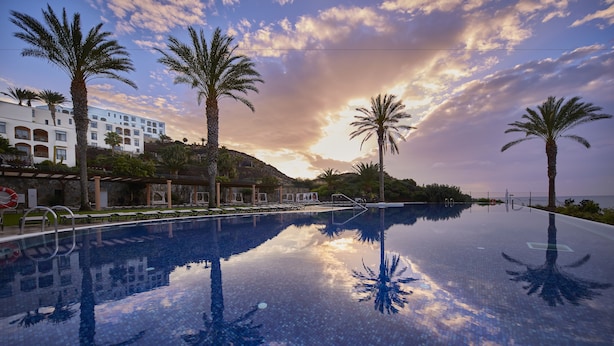 Una piscina con palmeras y un hotel al fondo.