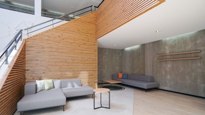 Un interior moderno con una escalera, sofás grises, una pequeña mesa redonda y una pared de concreto con listones de madera.