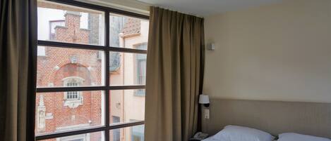 A hotel room with a large window, a bed, a bedside lamp, and a phone.