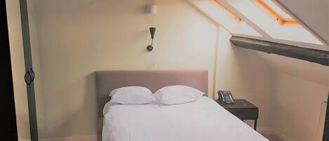 A bedroom with a bed, a bedside table, a telephone, and a skylight.
