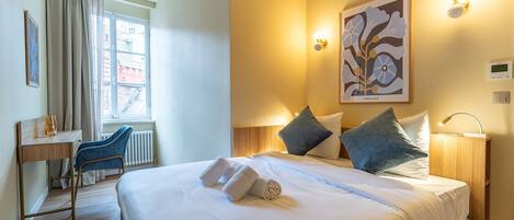 A hotel room with a bed, bedside table, lamp, and a window with curtains.