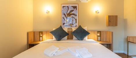 Une chambre d’hôtel avec un grand lit, deux tables de chevet, un appareil de climatisation, une œuvre d’art accrochée au mur et une armoire en bois.