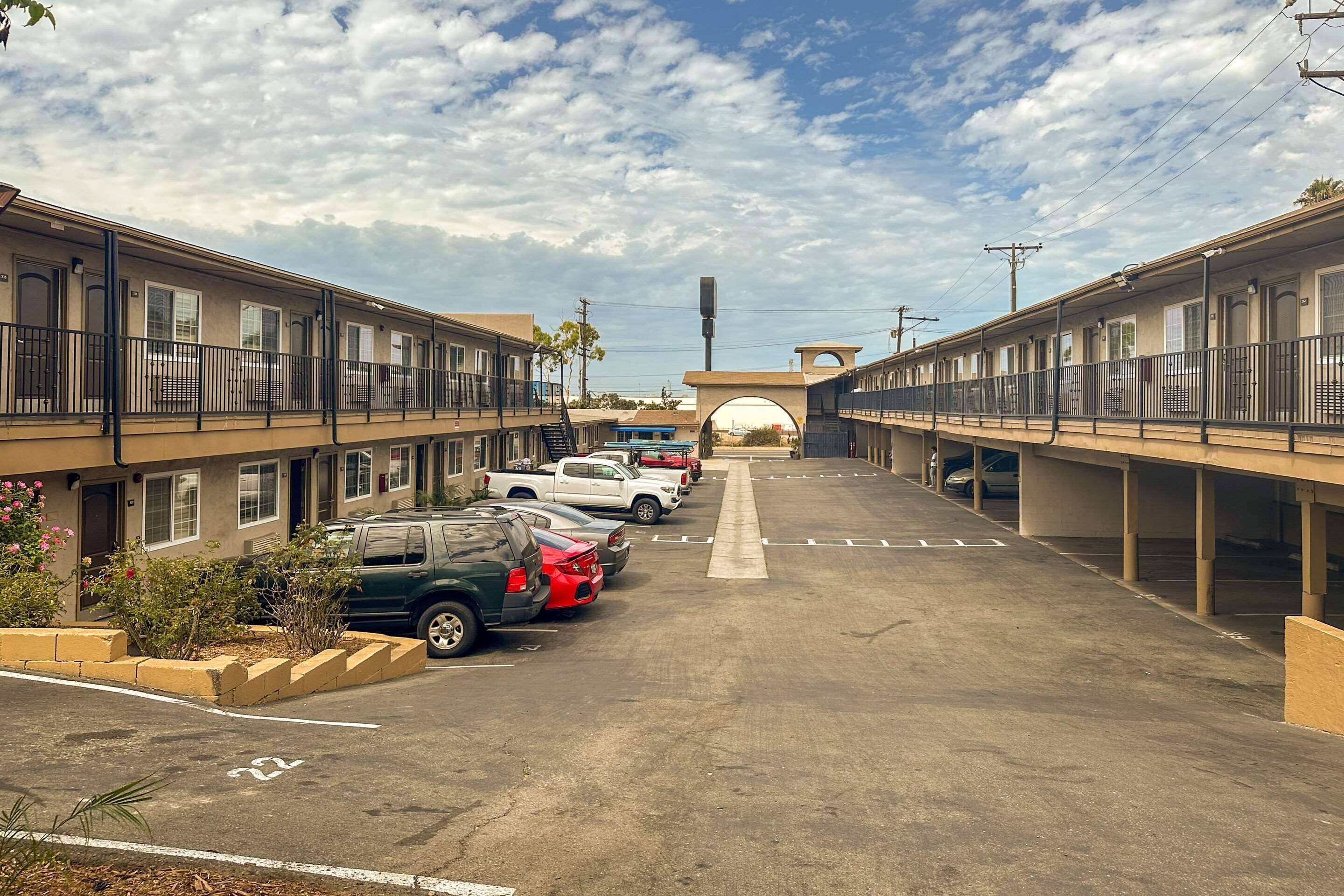 Un estacionamiento con varios autos estacionados, un edificio con balcones y un cielo despejado.