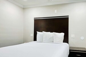 Una habitación de hotel con una cama grande, un cabecero oscuro y una mesita de noche pequeña.