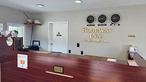 A reception area with a wooden reception desk, a clock displaying time in three different cities, and a sign for Rodeway Inn by Choice Hotels.
