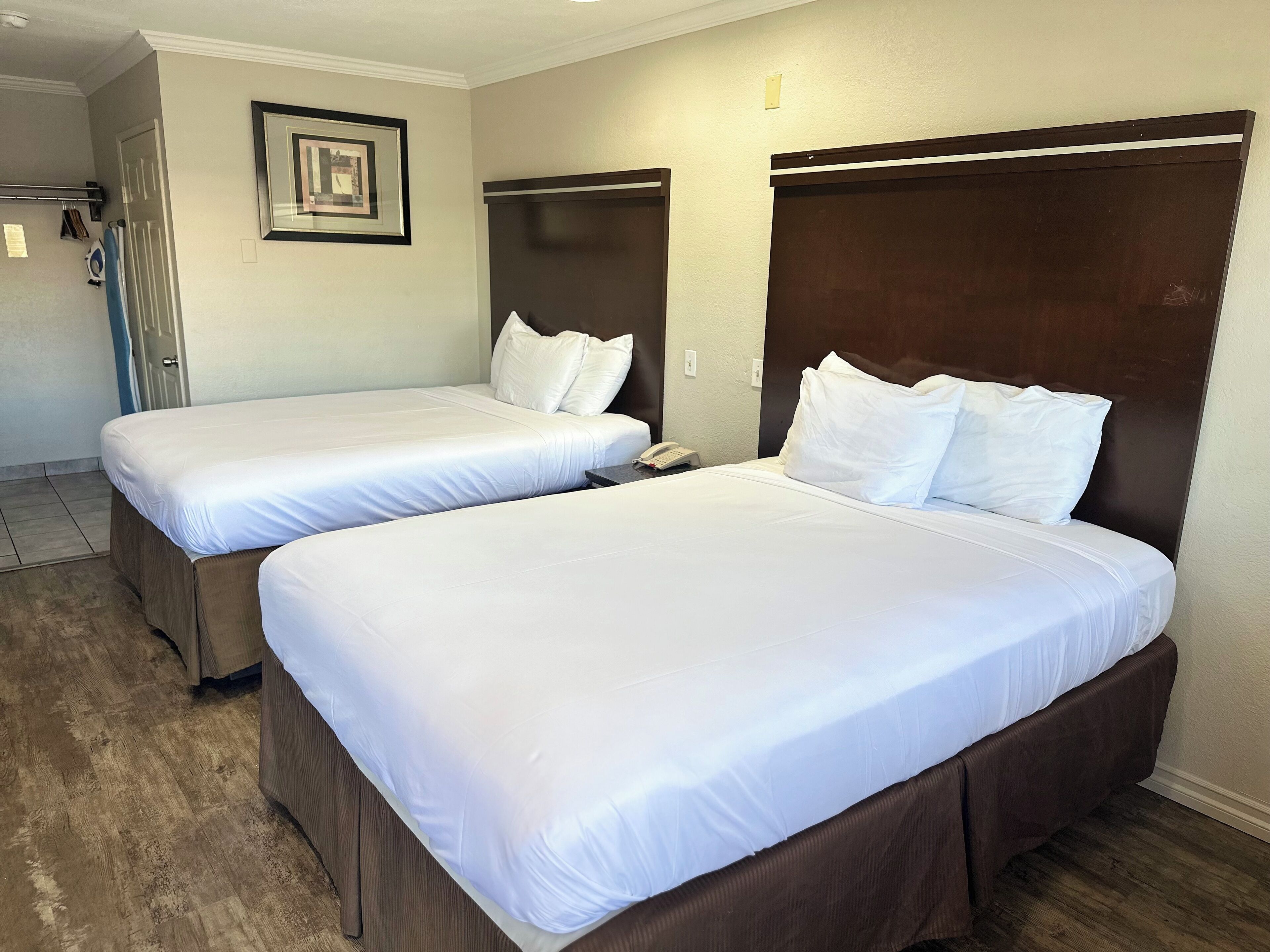 Hotelkamer met twee bedden, een houten hoofdbord, een ingelijst schilderij aan de muur en een telefoon op het nachtkastje.
