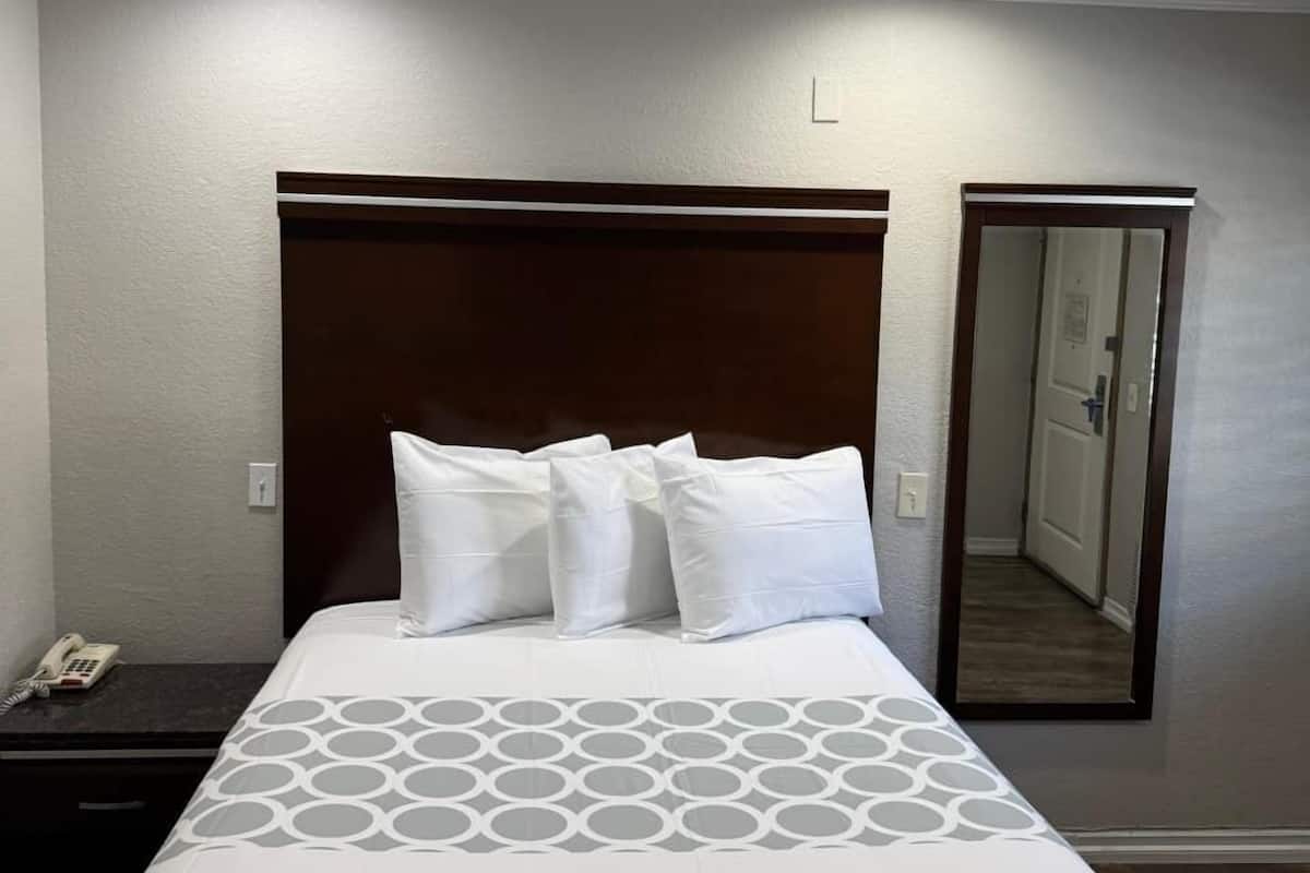 Habitación de hotel con una cama grande, una mesita de noche con teléfono y un espejo en la pared.