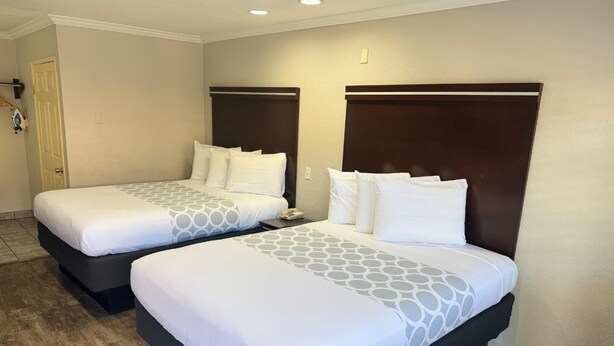 Two double beds with dark headboards and white bedding, a wooden floor, and a door on the left.
