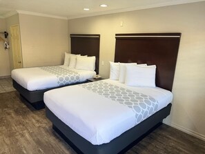 Dos camas dobles con cabeceros oscuros y ropa blanca, suelo de madera y una puerta a la izquierda.
