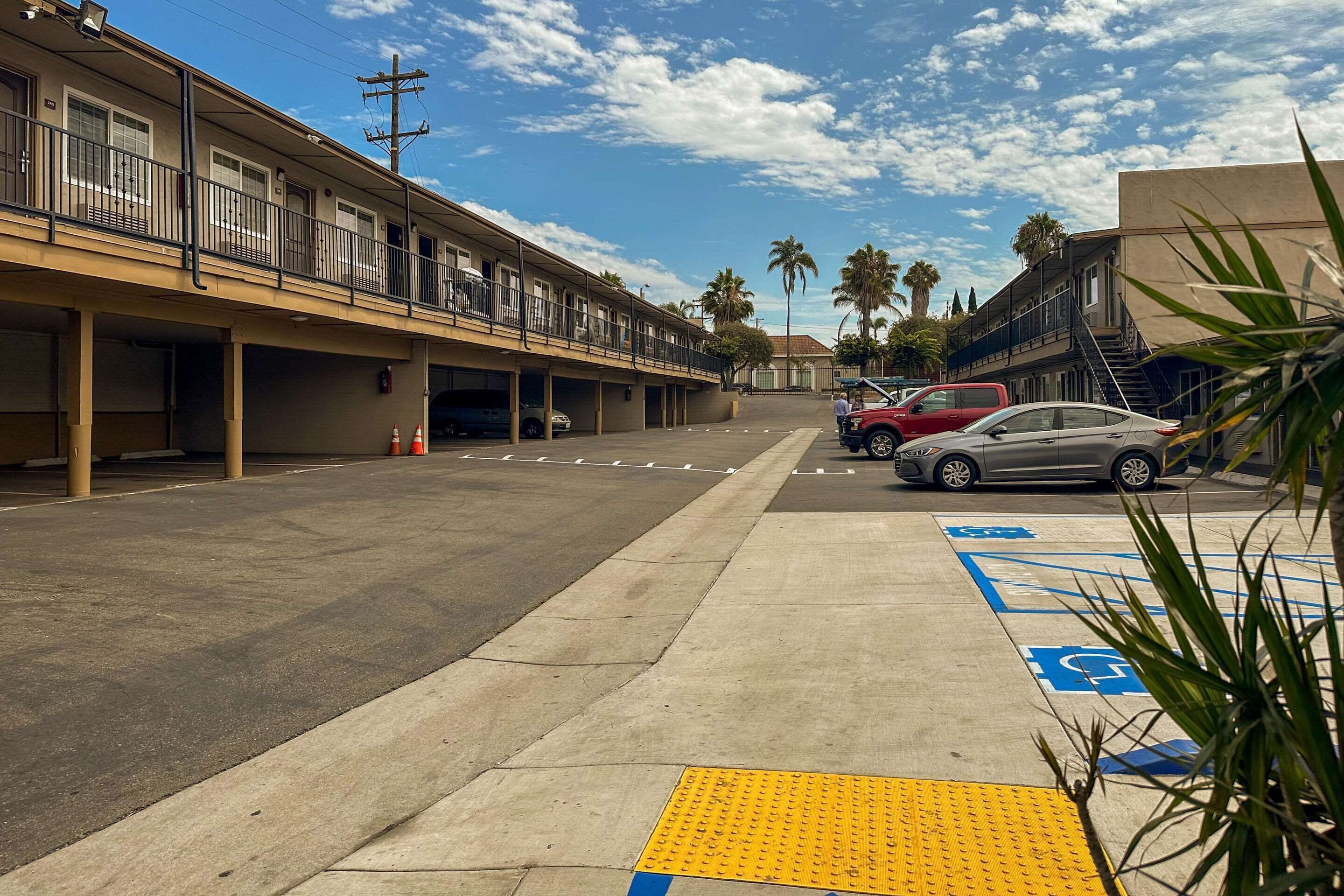 A parking lot with marked handicapped spaces, a building with a balcony, and palm trees in the background.