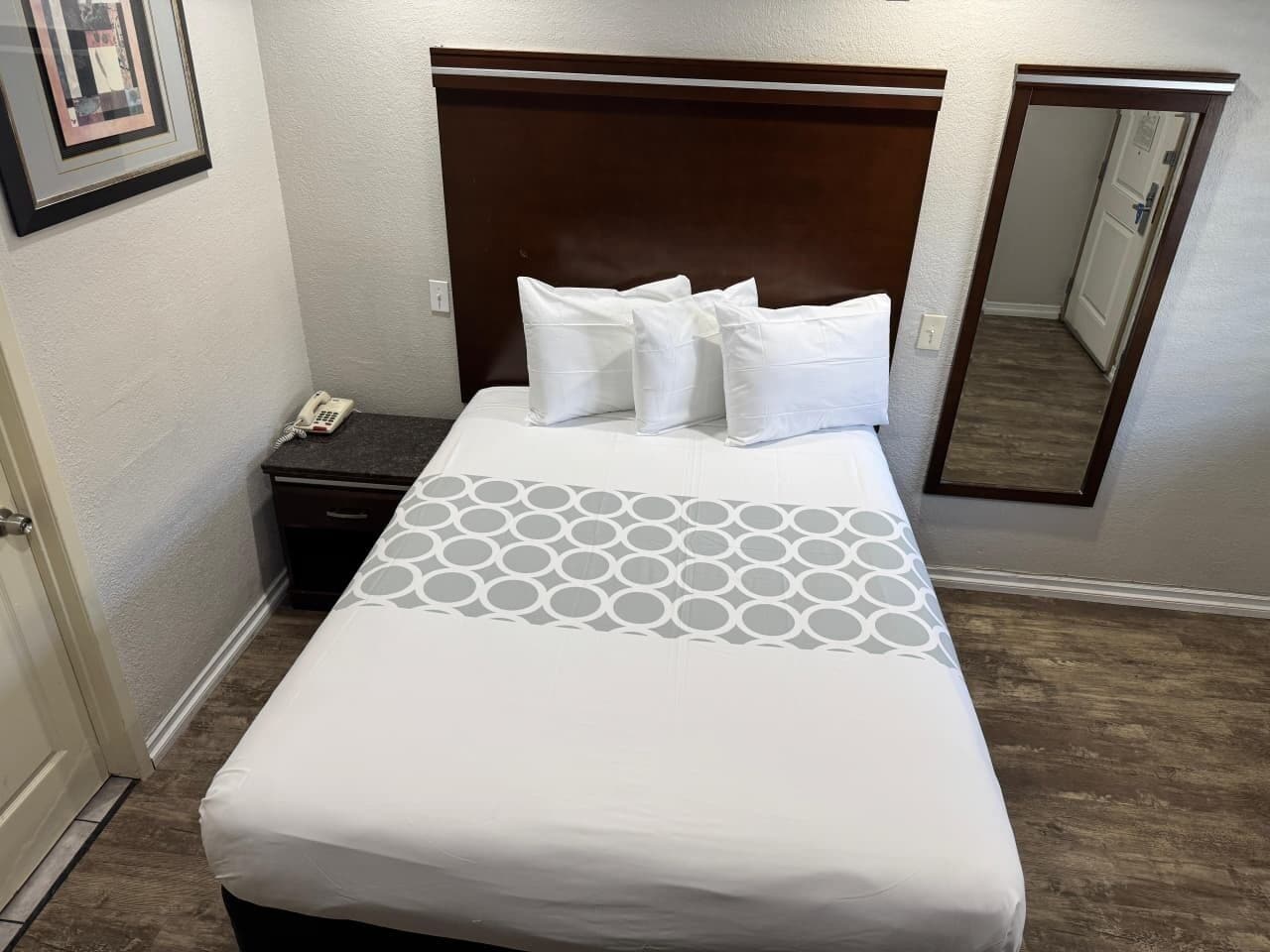 Una habitación de hotel con cama, mesita de noche, teléfono y espejo.