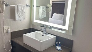A bathroom with a white sink, a mirror with a light, a hairdryer, and a towel rack.