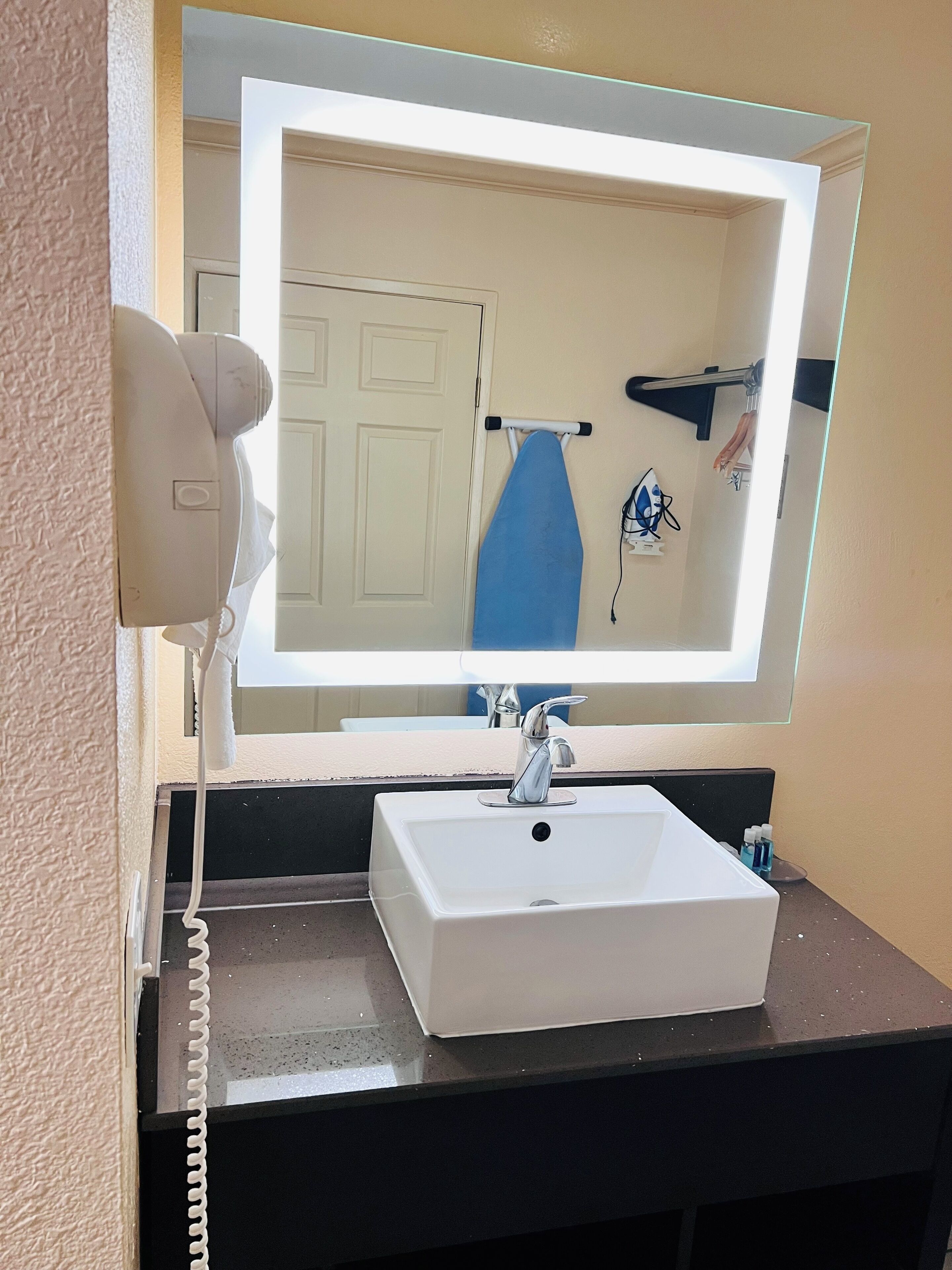 A bathroom with a white sink, a mirror, and a hairdryer on the wall.
