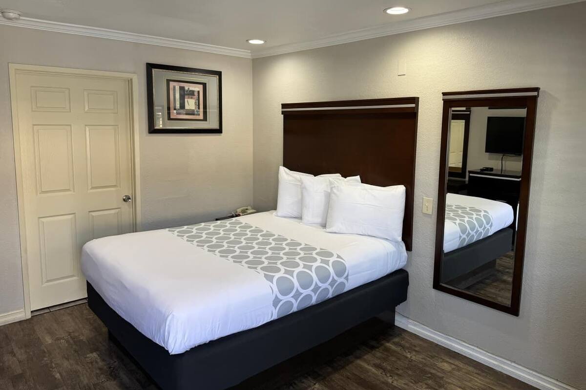 Habitación de hotel ordenada con una cama grande, un espejo junto a la cama y un cuadro en la pared.
