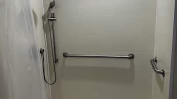 A shower area with a grab bar, a showerhead, and a drain.