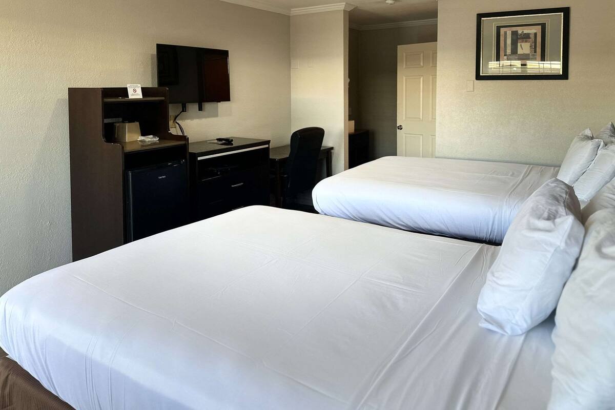 Una habitación de hotel con dos camas, un escritorio, una silla, un televisor y una puerta.