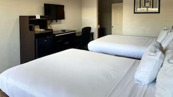 A hotel room with two beds, a desk, a chair, a TV, and a door.