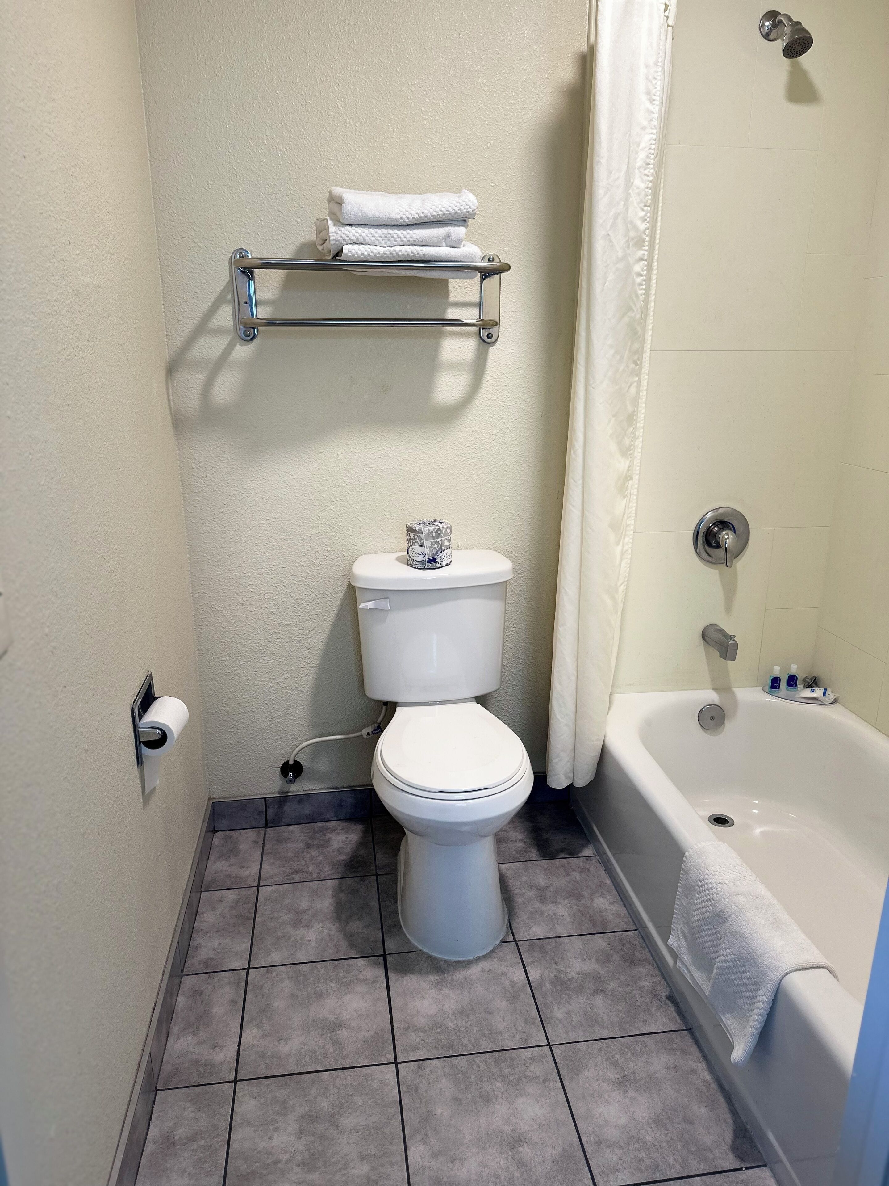 Un baño con inodoro, toallero con toallas dobladas, dispensador de papel higiénico, bañera y cortina de ducha.