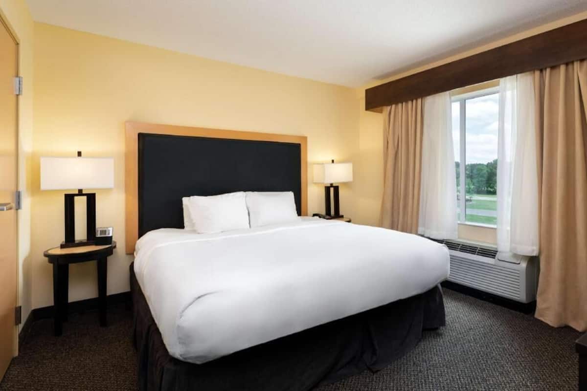 A hotel room with a large bed, two bedside tables with lamps, a window with curtains, and a radiator.