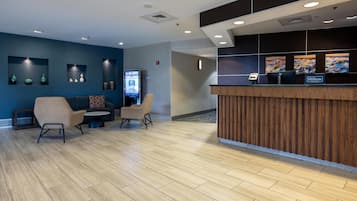 A hotel reception area with a wooden reception desk, two sofas, and a digital screen.