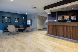 A hotel reception area with a wooden reception desk, two sofas, and a digital screen.
