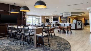 Um hall de hotel moderno com área de bar, assentos e uma grande TV de tela plana.