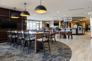 A modern hotel lobby with a bar area, seating arrangements, and a large flat-screen TV.