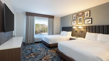 A hotel room with two beds, a desk, and a large window with curtains.