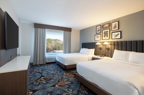 Une chambre d’hôtel avec deux lits, un bureau et une grande fenêtre avec des rideaux.