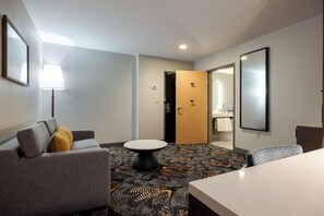 A hotel room with a grey sofa, a round table, a patterned carpet, and a mirror on the wall. - DoubleTree by Hilton Hotel Savannah Airport (Savannah)