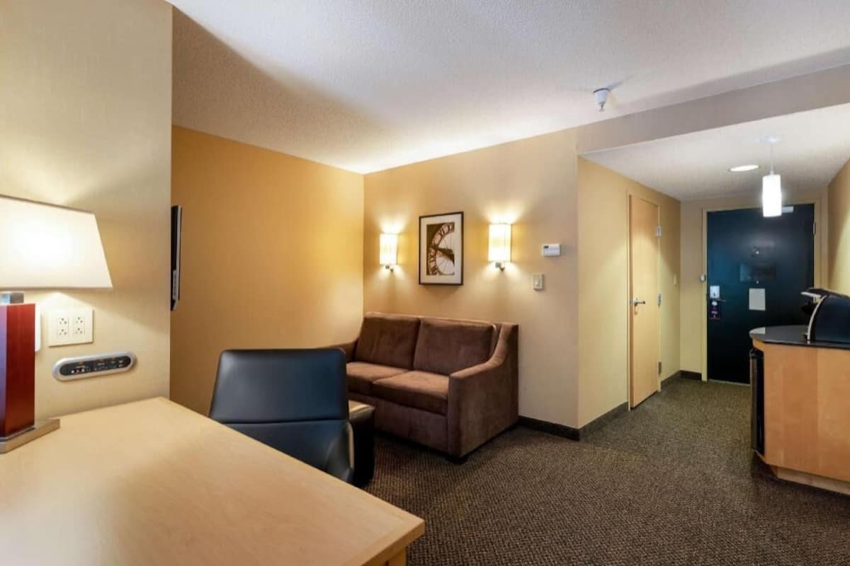 A hotel room with a desk, a sofa, a chair, a wall-mounted clock, and a reception desk.
