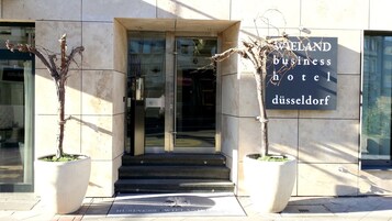L'ingresso dell'Hotel Business WIELAND a Düsseldorf, con una porta in vetro, una targa e due piante in vaso.