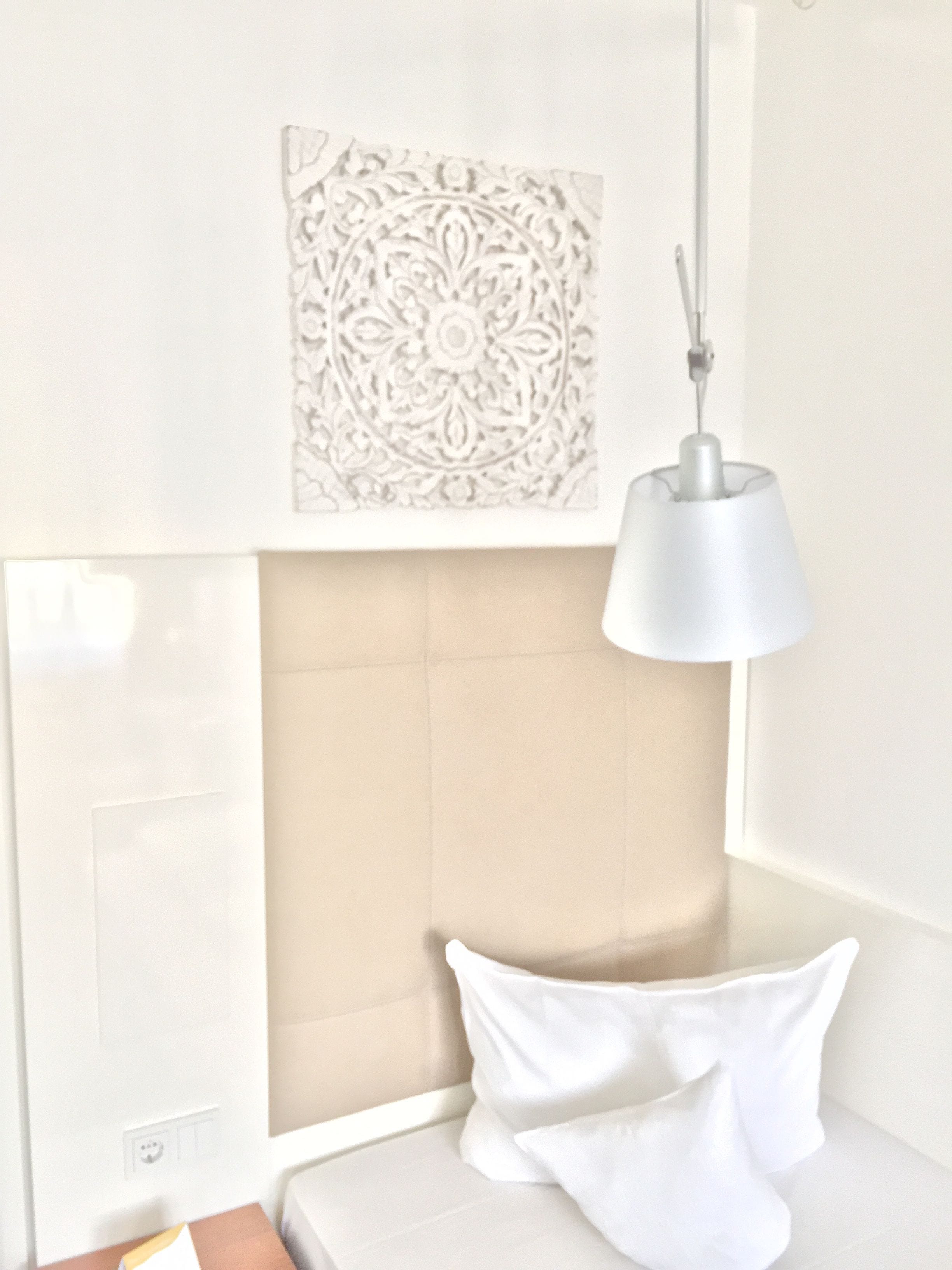 A neatly arranged room with a bed, a wall-mounted decorative panel, and a hanging lamp.