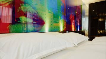 A modern hotel room with a large bed, a glass wall, and a colorful abstract artwork.