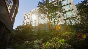 Een modern gebouw met meerdere verdiepingen, grote ramen en een tuin met diverse planten en bomen.