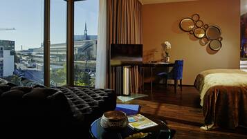 Habitación de hotel moderna con un ventanal grande que ofrece vistas a la ciudad, una cama cómoda, un escritorio con silla y una mesita con un cuenco decorativo.