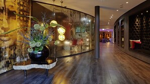 Een modern interieur met een houten vloer, een glazen wand met kunstwerken en een decoratieve plant als middelpunt.