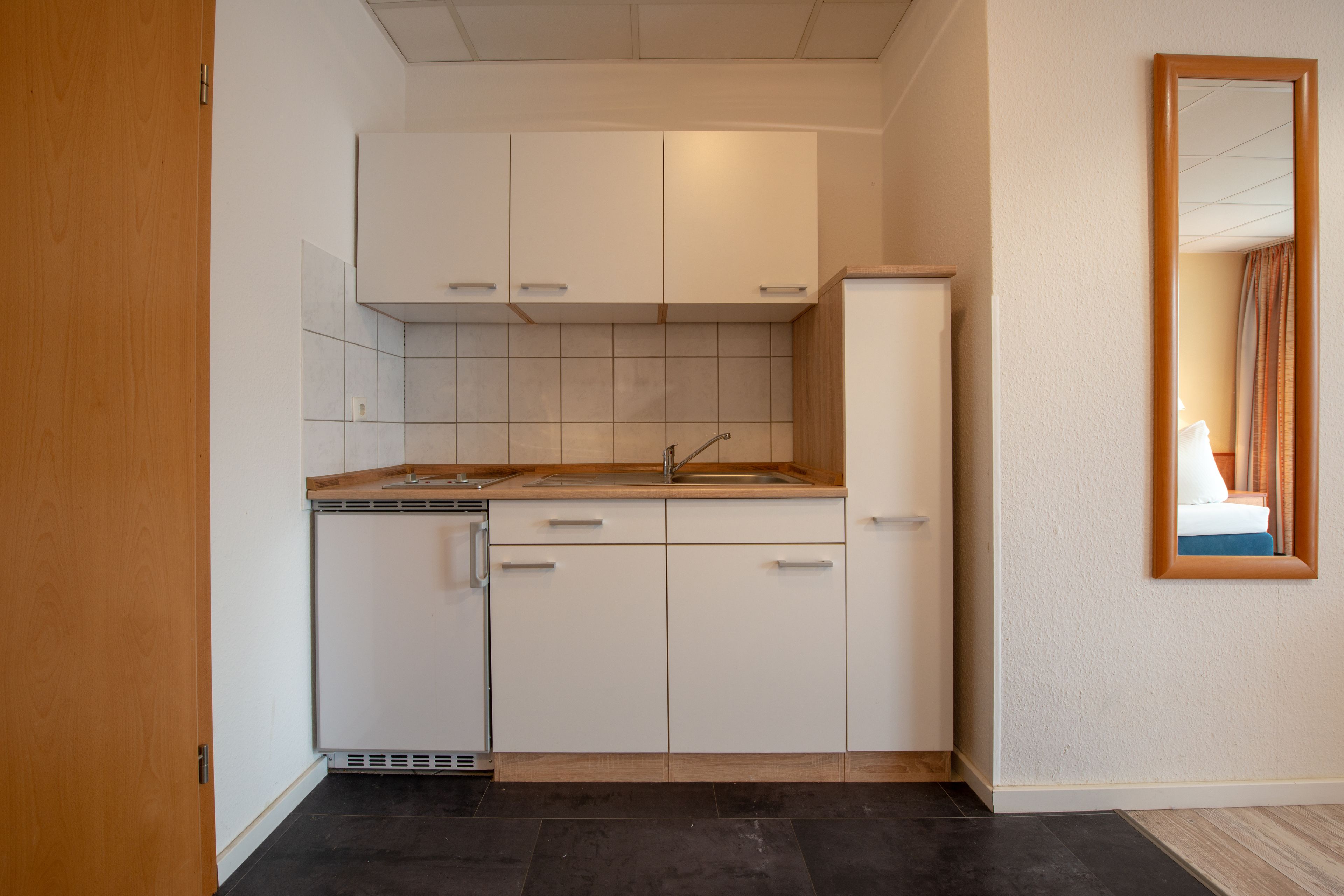 Een kleine keuken met witte kastjes, een geïntegreerde vaatwasser en een spoelbak.
