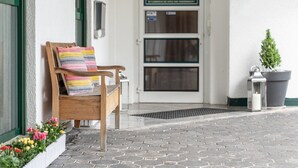 A wooden bench with a colorful cushion outside a building with a door and windows. - Boardinghouse Burgpark (Huerth)